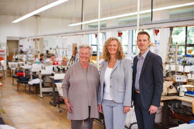Drei Personen der suprima Unternehmensgeschichte stehen laechelnd in der Produktionshalle in Bad Berneck, 2012