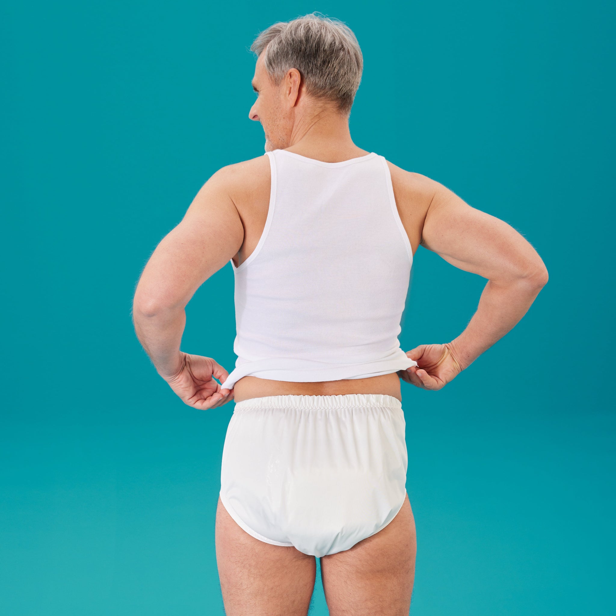 Rueckansicht eines Mannes im suprima PU-Slip 1287 in Weiss, er zieht das Shirt hoch und zeigt den Bund – Inkontinenzhose