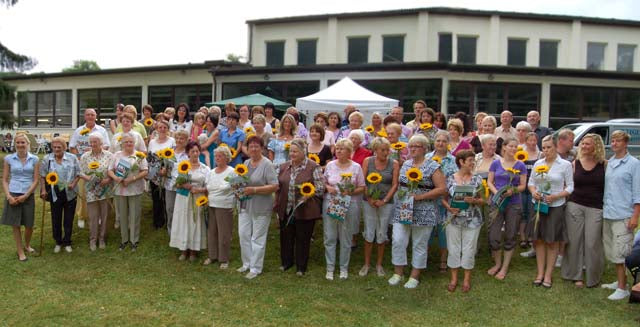 Grosse Gruppe von suprima Mitarbeitenden mit Sonnenblumen beim 75-jaehrigen Firmenjubilaeum 2010 vor dem Firmengebaeude in Bad Berneck
